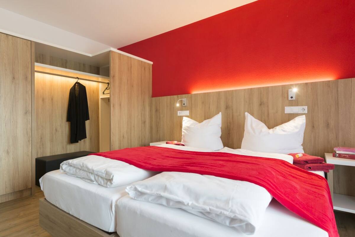 A hotel room with a bed, a bench, a red wall, and wooden paneling.
