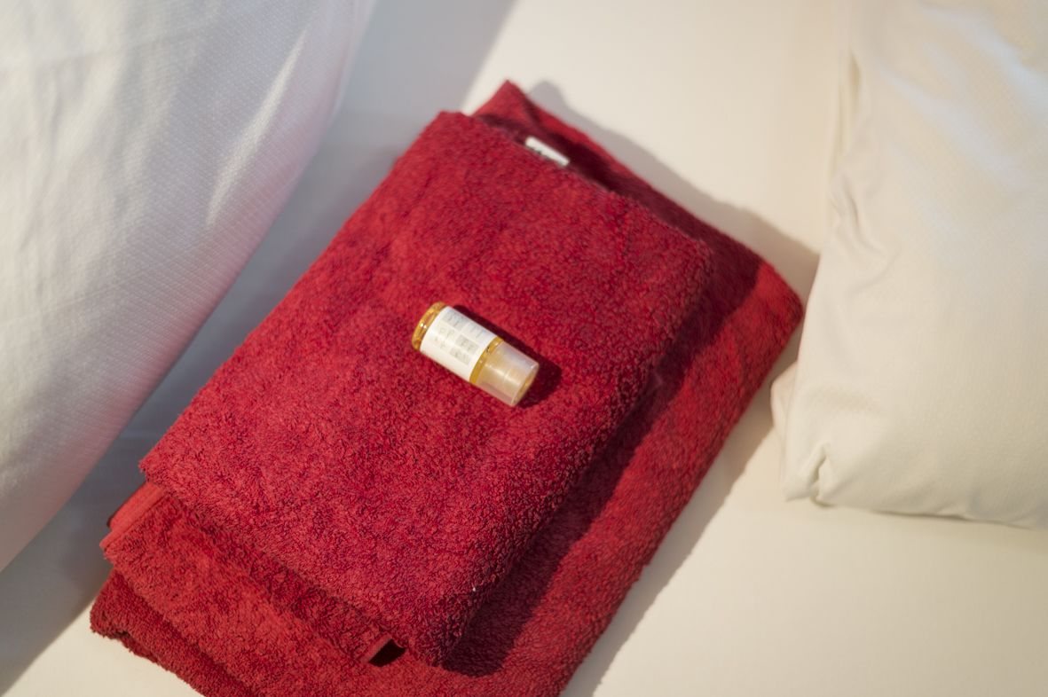A red towel folded on a bed with a bottle on top.