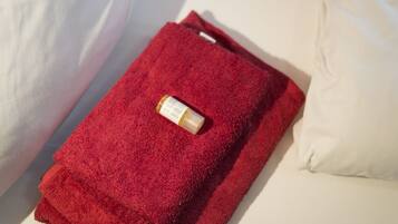 A red towel folded on a bed with a bottle on top.