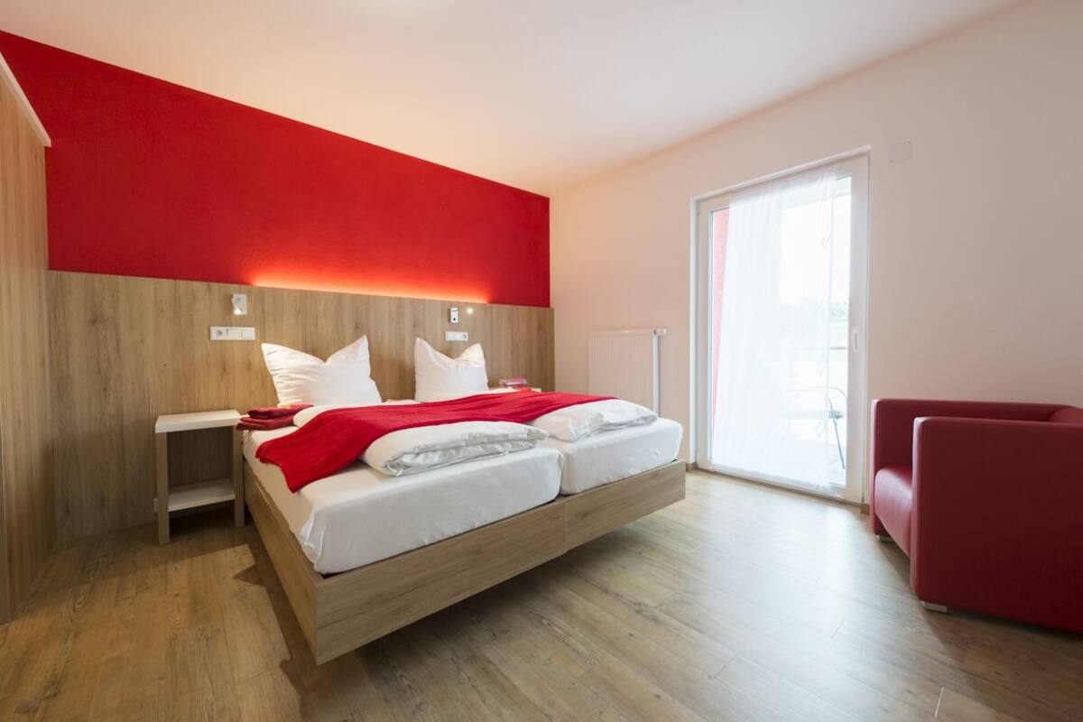 A modern bedroom with a bed, a red accent wall, and a red sofa.
