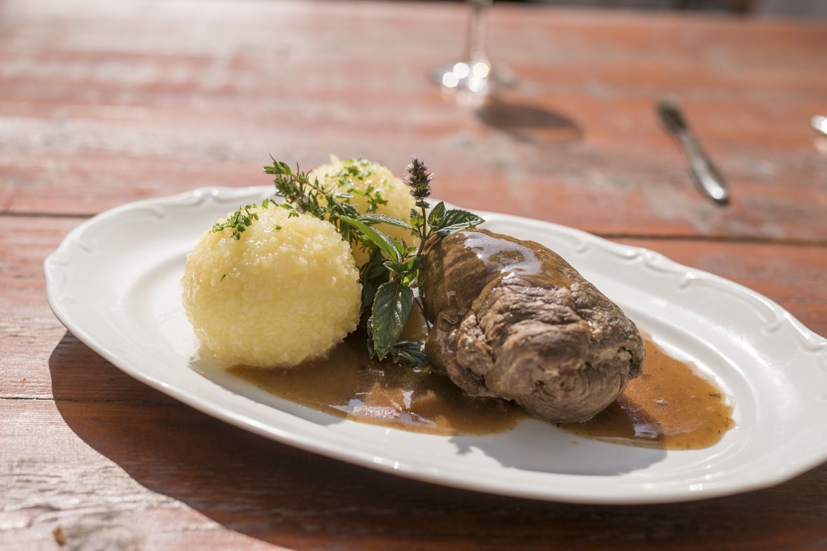 A plate with a meat dish and mashed potatoes, garnished with herbs, on a wooden table.