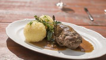 A plate with a meat dish and mashed potatoes, garnished with herbs, on a wooden table.