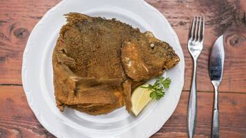 A plate with a breaded fish, lemon wedge, and parsley on a wooden table.