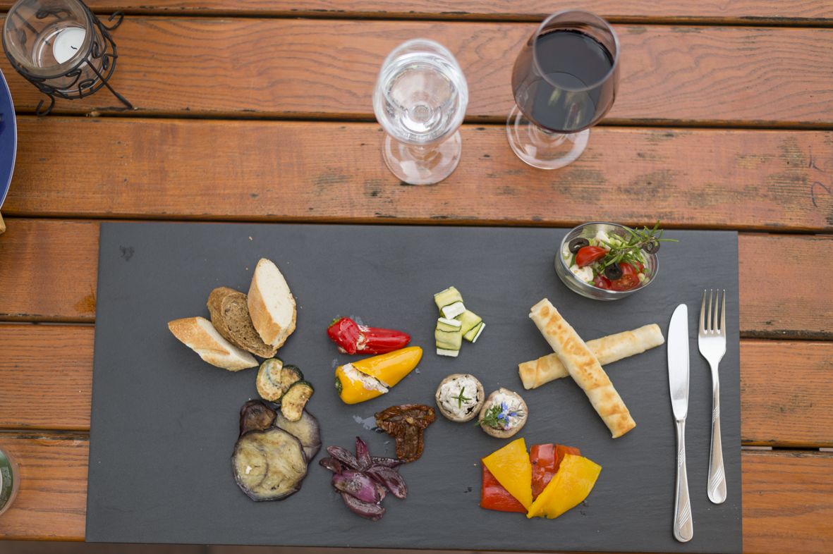 A wooden table with a slate serving board holding various foods, a glass of water, and a candle.
