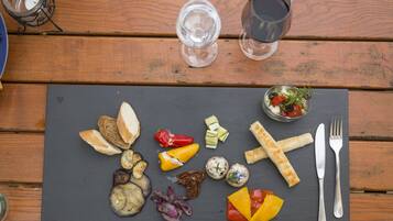 A wooden table with a slate serving board holding various foods, a glass of water, and a candle.