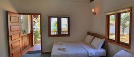 Una habitación con dos camas, techo de madera y ventana con vistas a palmeras.