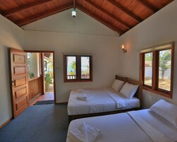 A room with two beds, a wooden ceiling, and a window with a view of palm trees.