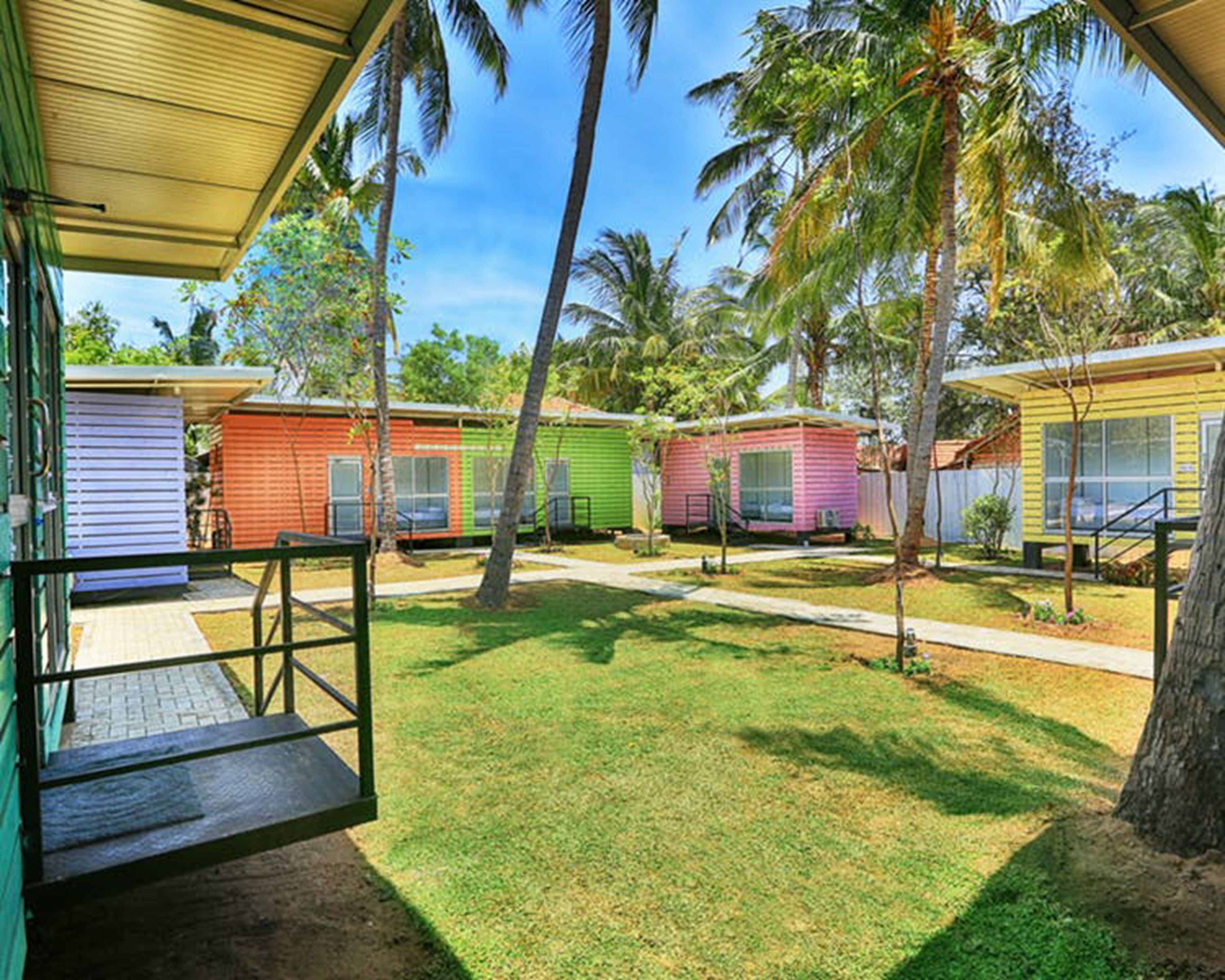 A row of colorful mobile homes with a grassy yard and palm trees.
