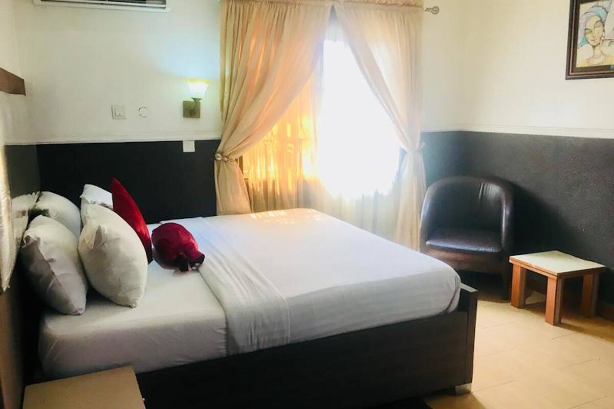 A hotel room with a large bed, a desk, a chair, and a window with curtains.