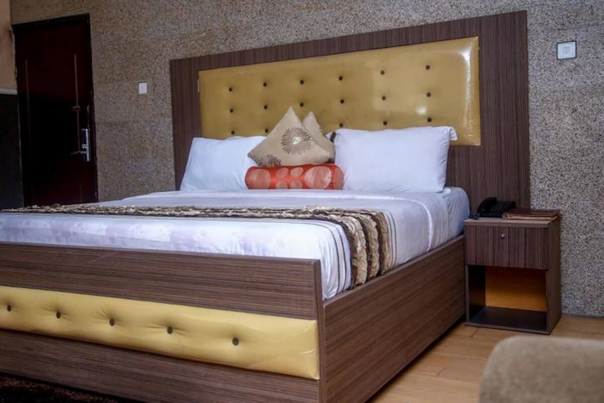 A neatly made bed with a tufted headboard, a bedside table with a phone and a book, and a small wooden cabinet.