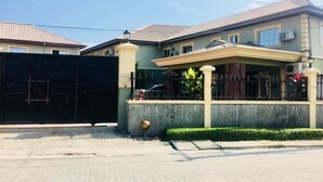 A two-story house with a gated entrance, a covered porch, and a well-maintained lawn. - Le Brigadier Hotel (Lekki)