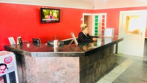 A reception desk with a television mounted above it, a glass partition, and a door with a bright light. - Le Brigadier Hotel (Lekki)