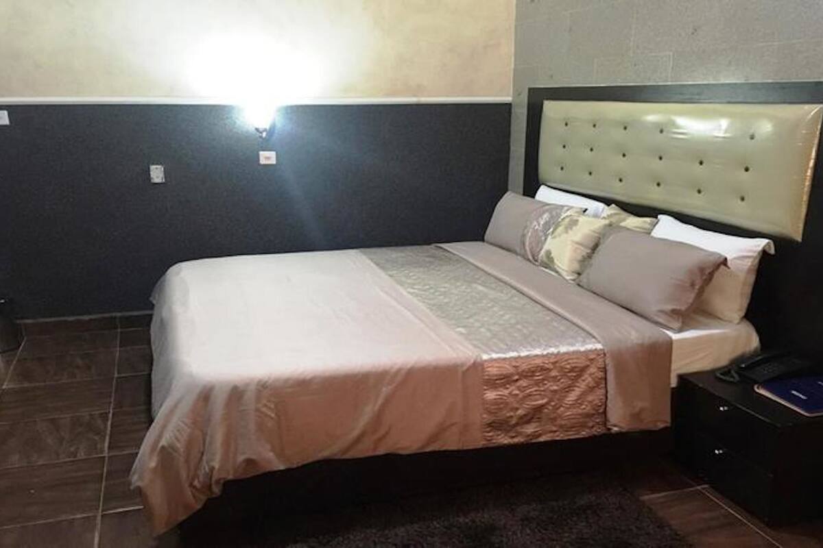 A bedroom with a bed, a nightstand, and a wall-mounted light.