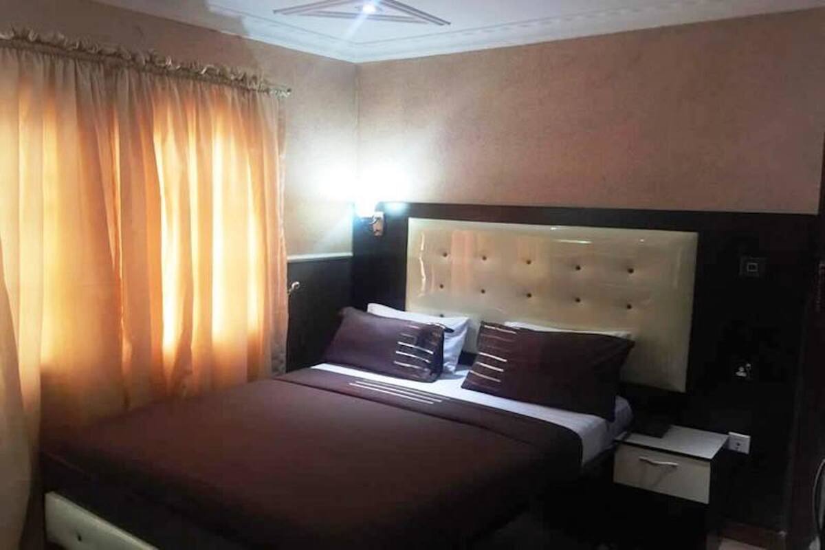 A hotel room with a large bed, a nightstand, and a window with curtains.