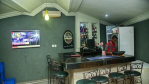 A bar area with a counter, stools, a television displaying a sports channel, and shelves with bottles. - Le Brigadier Hotel (Lekki)