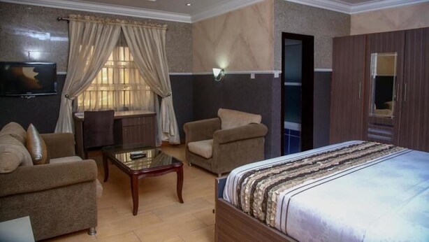 A hotel room with a bed, two armchairs, a small table, and a TV. - Le Brigadier Hotel (Lekki)