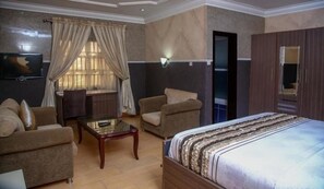 Une chambre d’hôtel avec un lit, deux fauteuils, une petite table et un téléviseur.