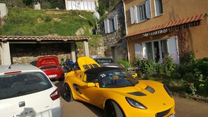 A street with parked cars, including a yellow sports car, a red car, and a white car. There is a building with a sign that reads "SAN-LARENZU". - San Larenzu (Aullène)