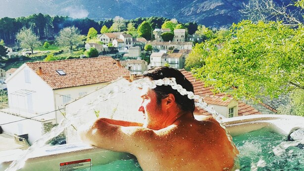 A person in a hot tub with a mountainous village in the background. - San Larenzu (Aullène)