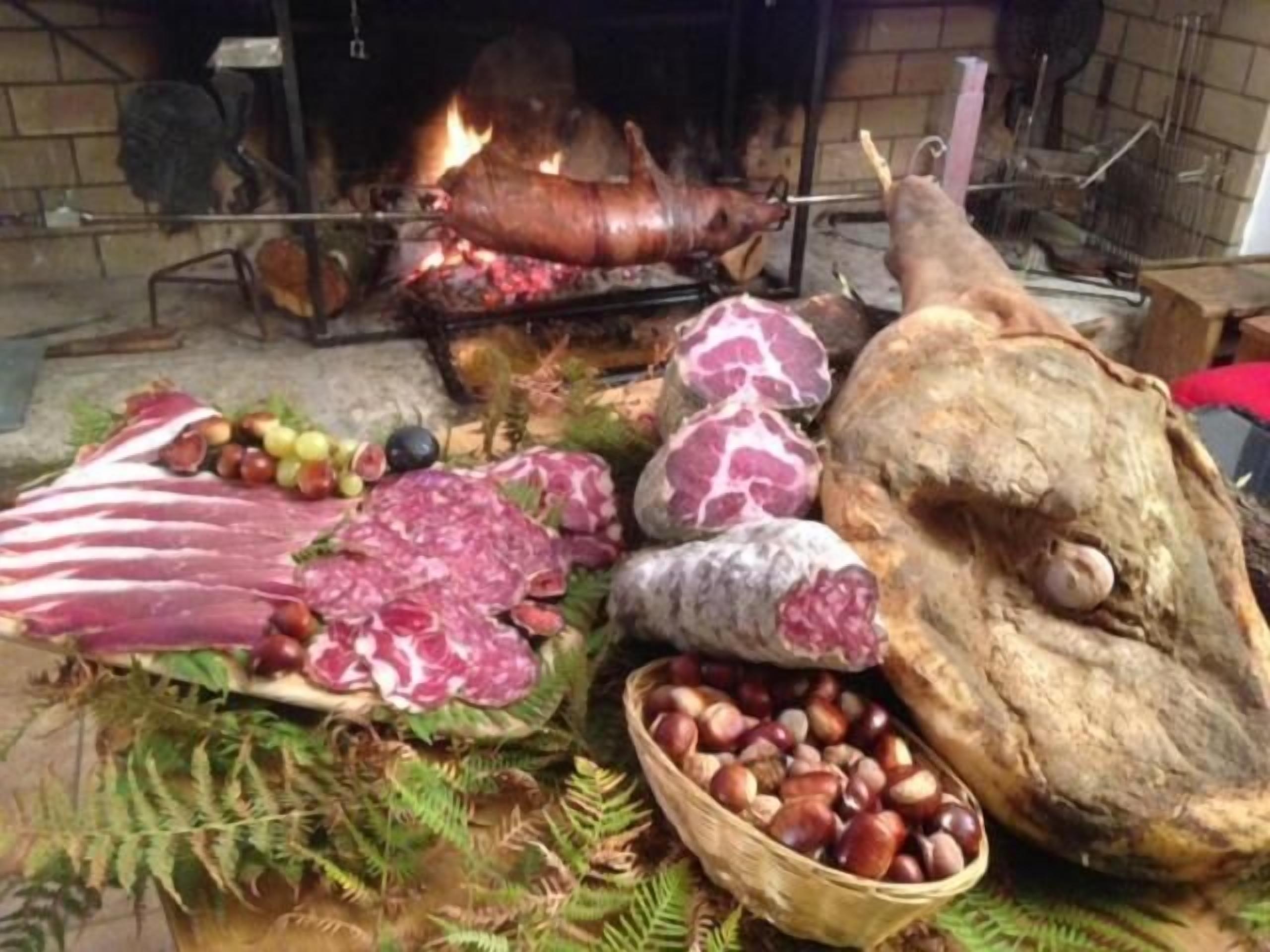Un montaje tradicional para cocinar al aire libre, con un cerdo asado entero, diversas carnes y una cesta de castañas.