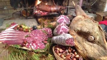 Un montaje tradicional para cocinar al aire libre, con un cerdo asado entero, diversas carnes y una cesta de castañas.
