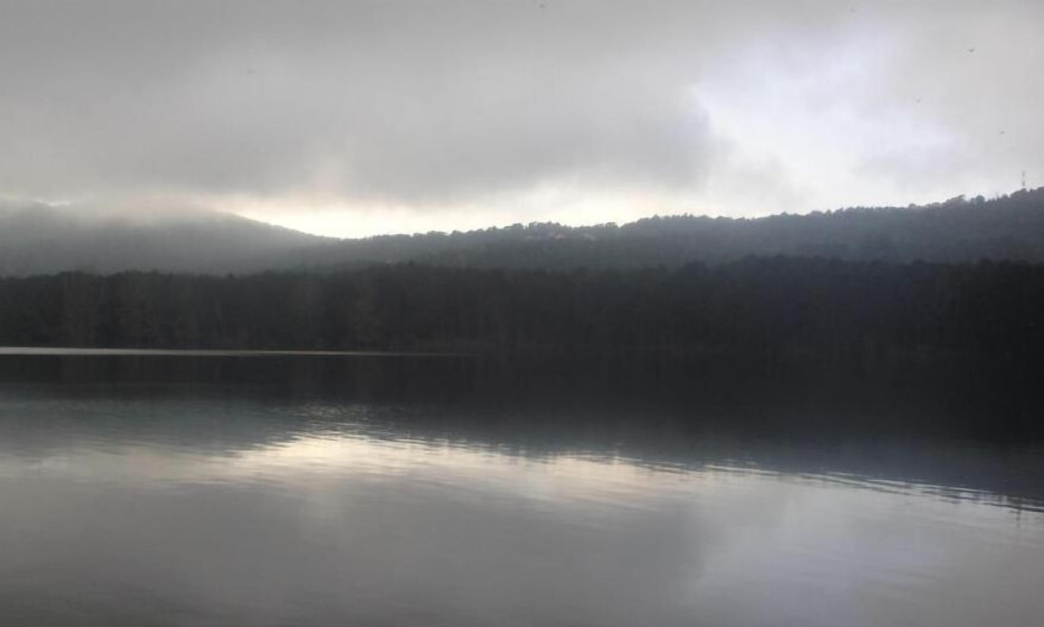 Un lac paisible, avec une montagne boisée en arrière-plan.