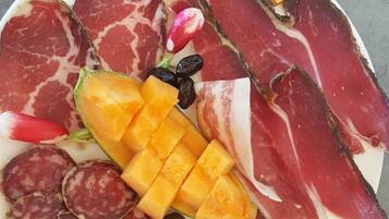 Een bord met diverse soorten vleeswaren, waaronder salami en parmaham, geserveerd met augurken, een mango en olijven.