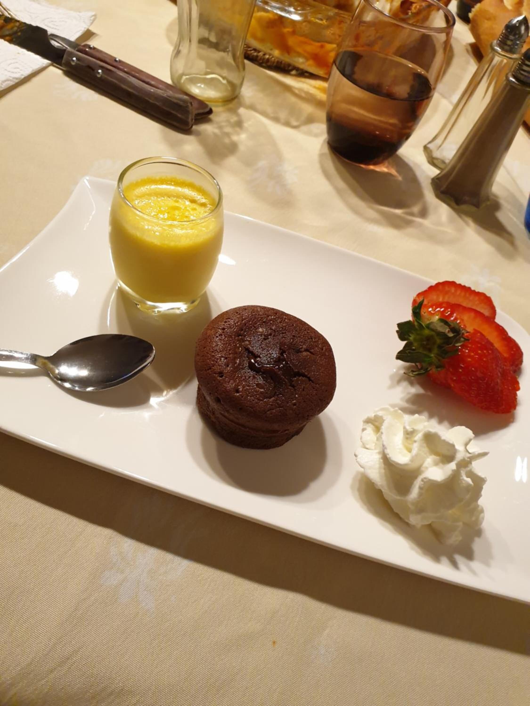 A dessert plate with a chocolate muffin, a scoop of vanilla ice cream, a strawberry, and whipped cream.