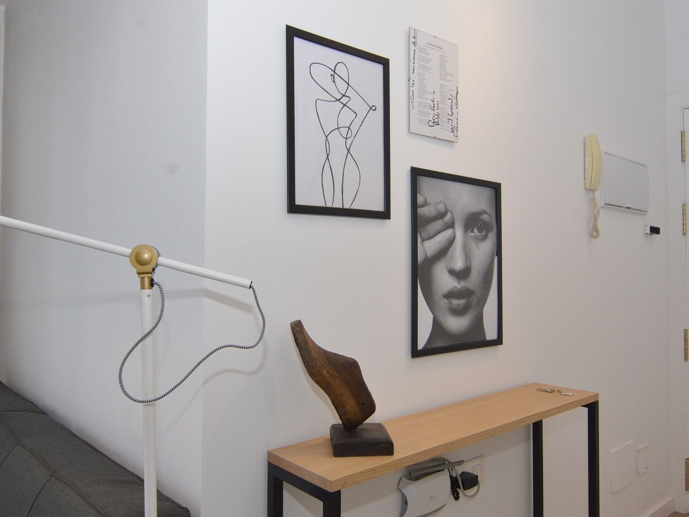 Ein Flur mit weißer Wand, einem gerahmten abstrakten Kunstwerk, einem gerahmten Foto und einer Holzskulptur auf einem Tisch.
