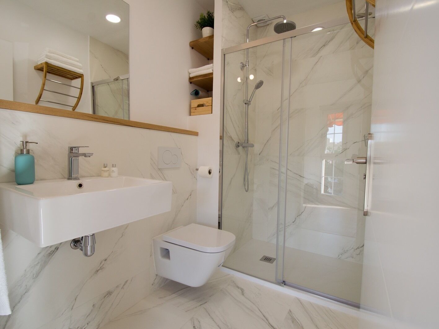 A modern bathroom with a marble floor, a white sink, a toilet, and a glass-enclosed shower.