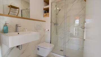 A modern bathroom with a marble floor, a white sink, a toilet, and a glass-enclosed shower.
