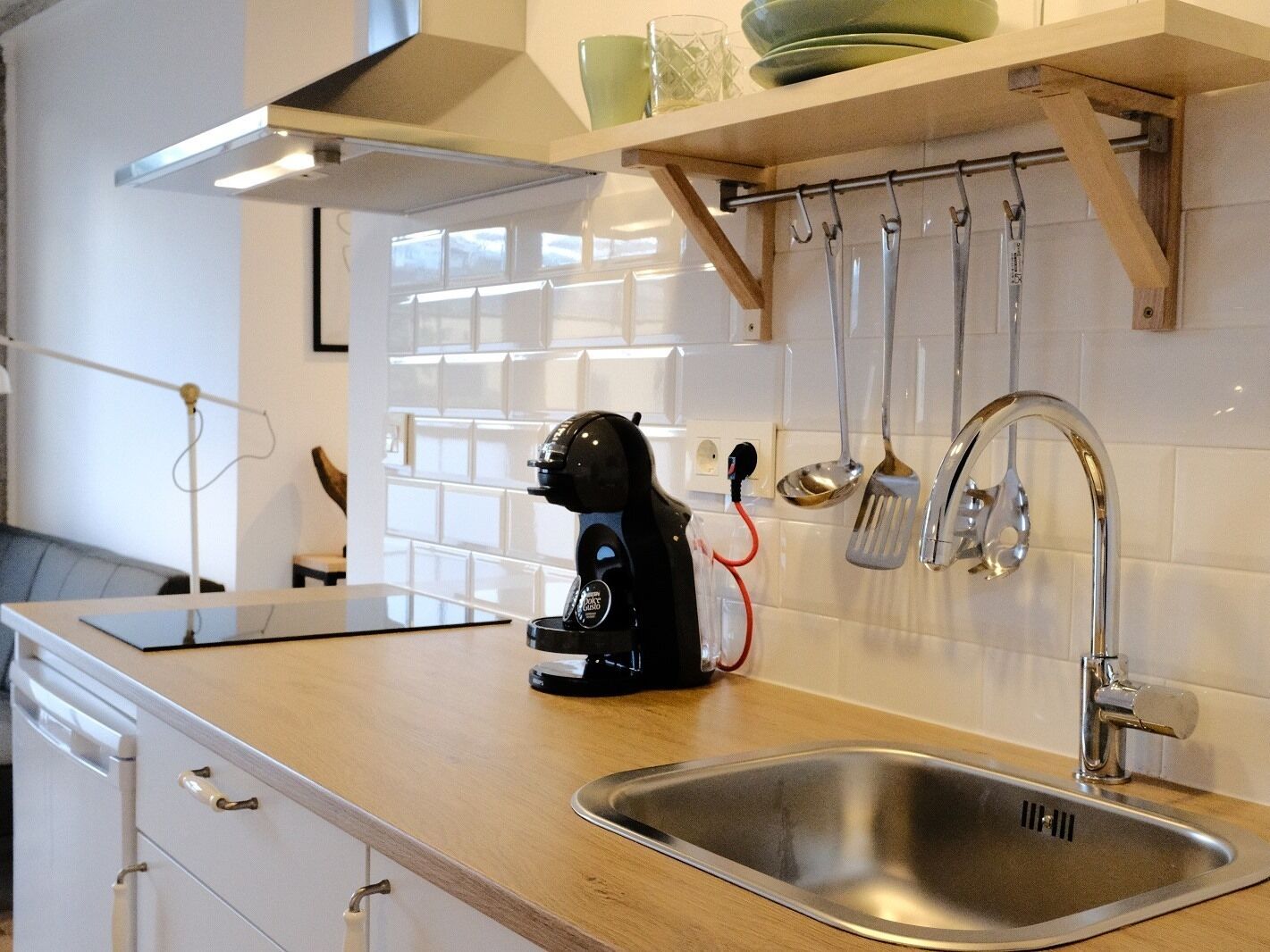 Een keuken met een roestvrijstalen spoelbak, een koffiezetapparaat, en keukengerei dat aan een rek hangt.