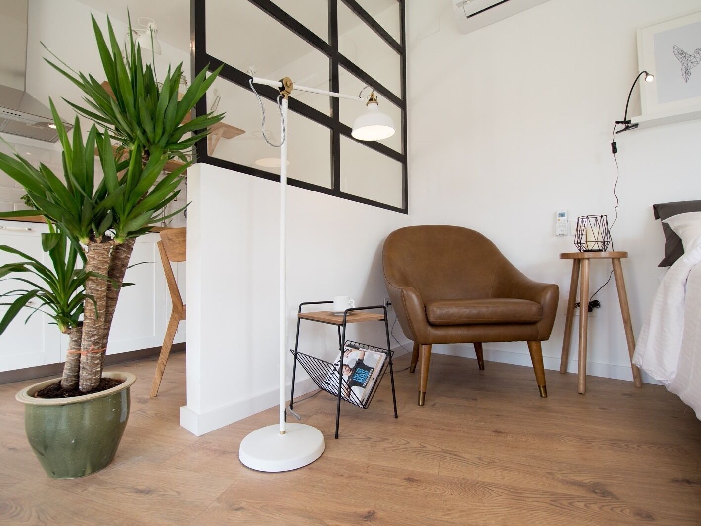 Una sala moderna con suelo de madera, un sillón de cuero marrón, una lámpara de pie blanca, una planta en maceta verde y un mueble para revistas.