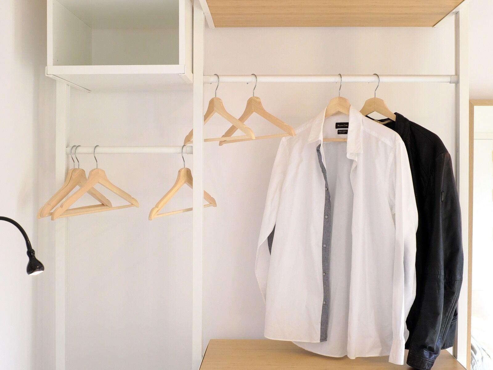 Un armario con perchas de madera y una camisa blanca colgada.