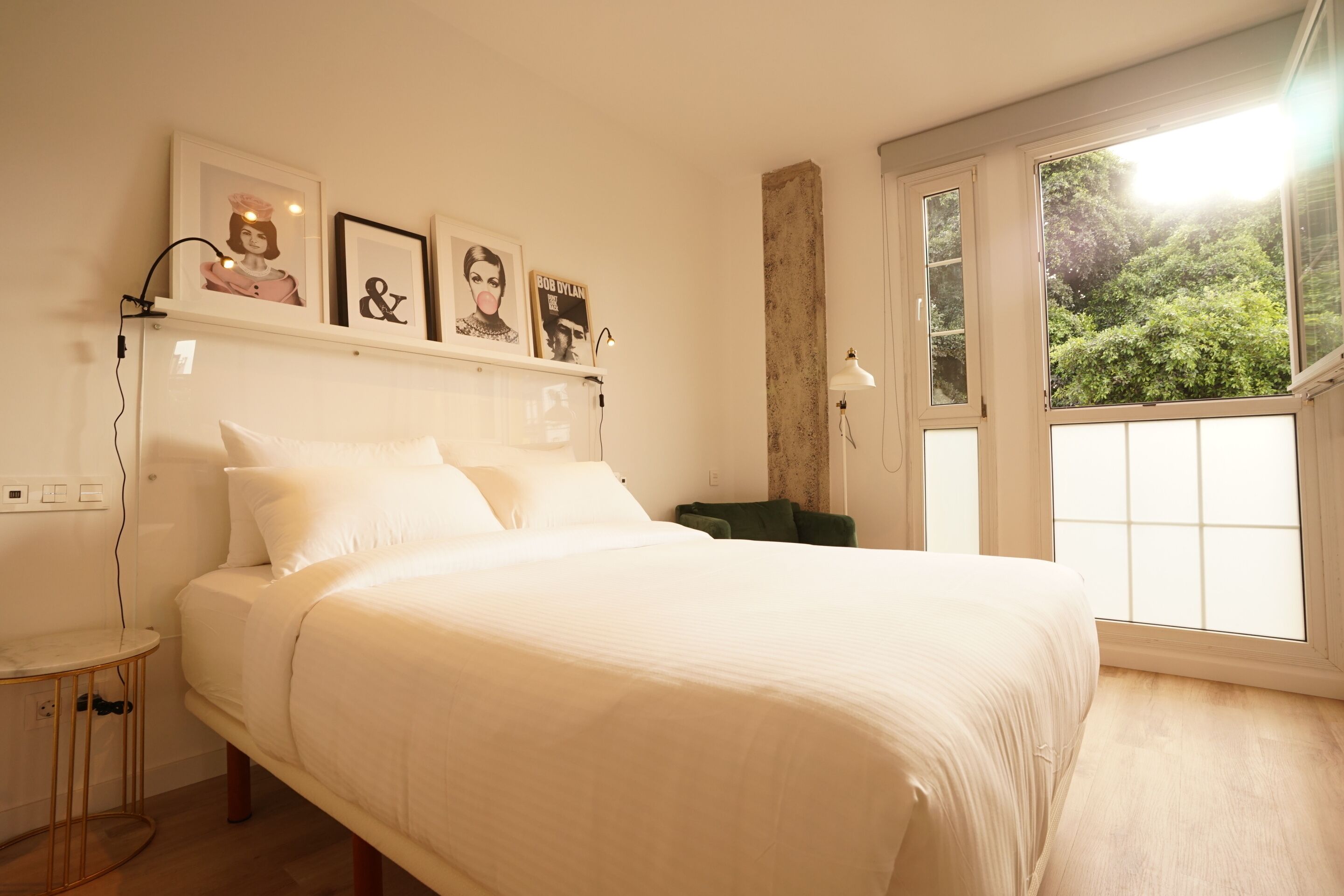 Una camera da letto con un letto grande, un comodino, una poltrona verde e una finestra che si affaccia sul verde.