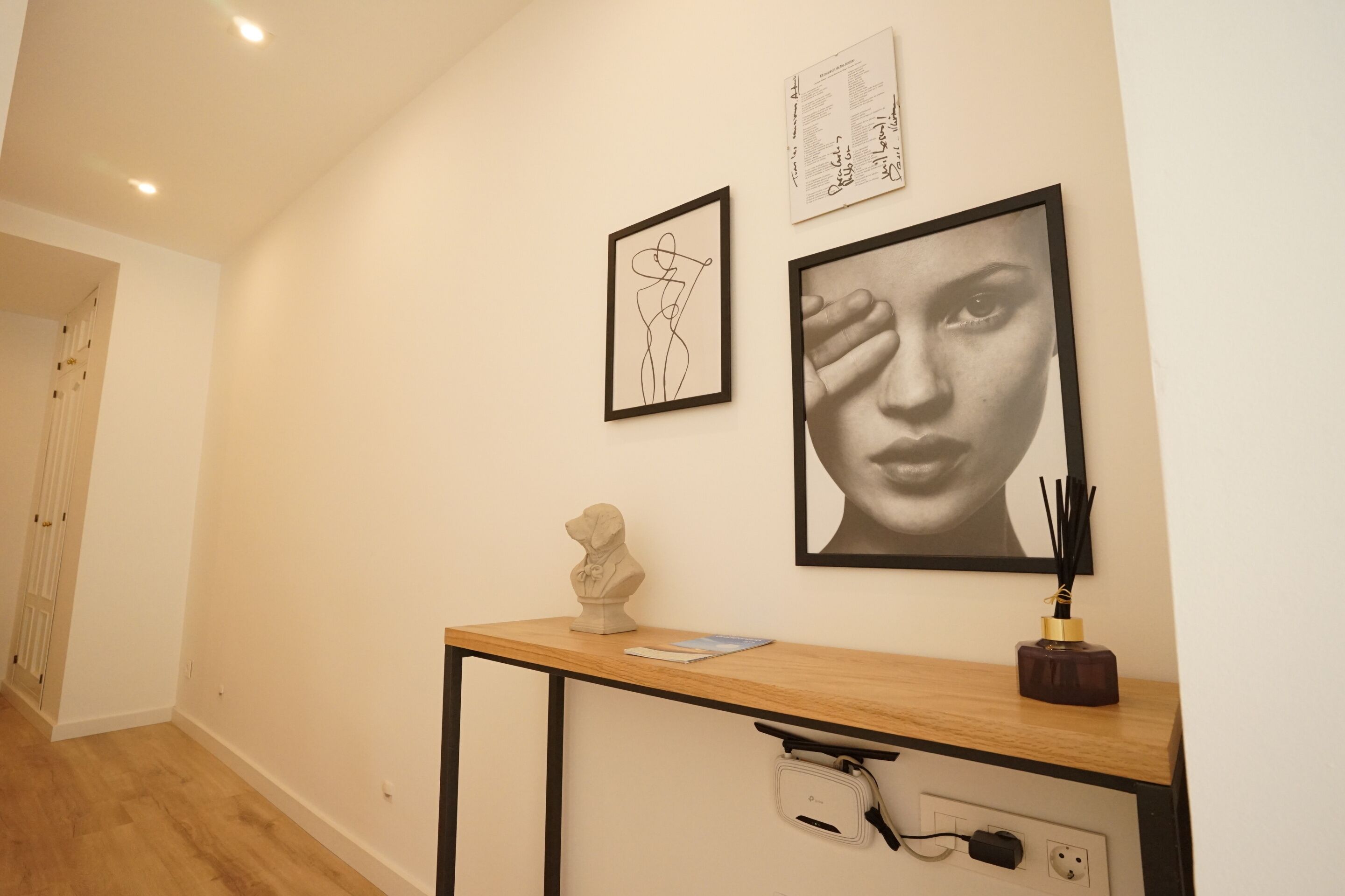 A hallway with a wooden desk, a bust sculpture, and two framed artworks on the wall.