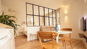 A modern kitchen with white cabinets, a wooden dining table, and chairs. There is a large mirror on the wall, a potted plant, and a vase on the table. - The Stay Las Palmas (Las Palmas de Gran Canaria)