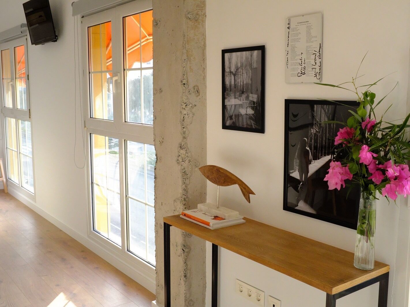 Un pasillo con ventanas amplias, una mesa de madera con un florero y obras de arte en las paredes.