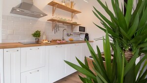 A modern kitchen with white cabinets, a wooden countertop, a stainless steel range hood, and a microwave. There are jars on a shelf, a plant, and kitchen utensils hanging on the wall. - The Stay Las Palmas (Las Palmas de Gran Canaria)