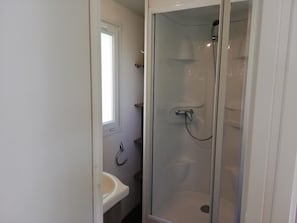Een badkamer met een douchecabine van glas, een wastafel en een raam.
