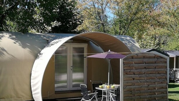 Une petite structure semi-ouverte dotée d’une porte en verre, d’une table de patio et d’une chaise.