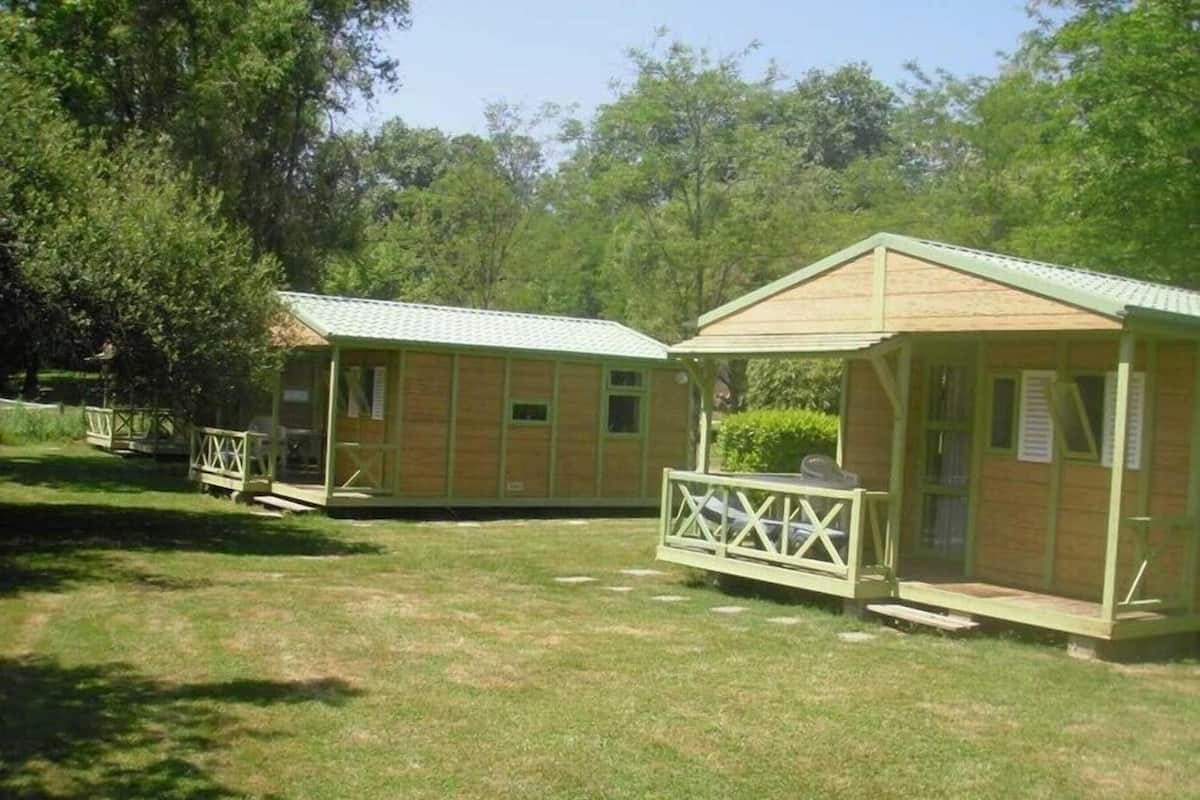 Deux cabanes en bois, chacune dotée d’une véranda attenante, entourées d’herbe et d’arbres.