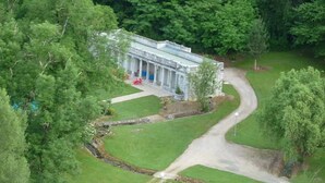 Un bâtiment de style architectural classique, entouré d’une végétation luxuriante et bordé d’un sentier sinueux.