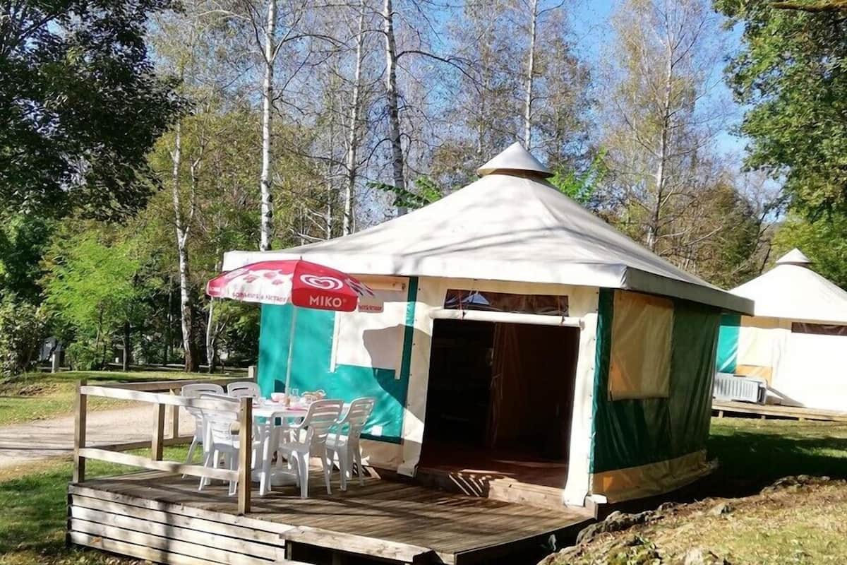 Une petite construction d’un seul étage, dotée d’un toit à deux versants, d’un espace extérieur abrité avec des chaises en plastique et une table, et d’une entrée en forme de tente.