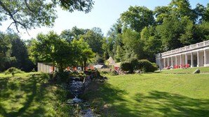 Un espace extérieur paisible, agrémenté d’un petit ruisseau, d’une végétation luxuriante et d’un bâtiment classique doté de colonnes.