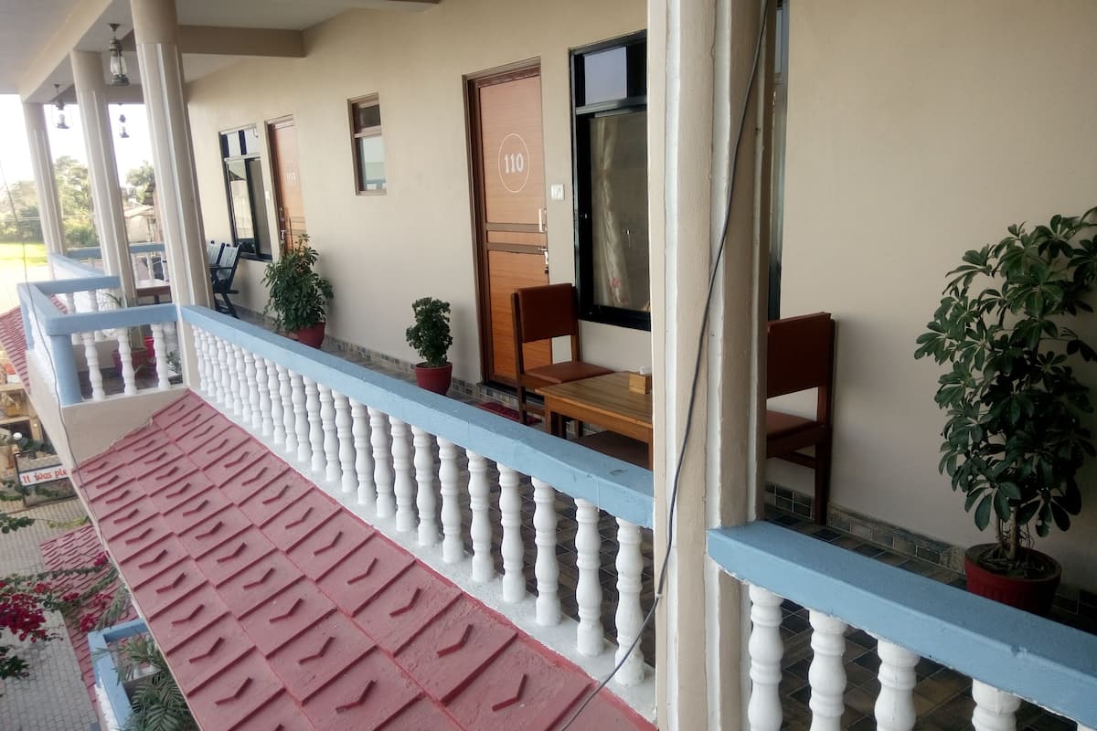 Een overdekt balkon met een rode en blauwe balustrade, planten in potten, en een houten tafel met stoelen.