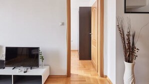 Uma sala de estar moderna com uma televisão de tela plana em um suporte branco, piso de madeira e um vaso branco com plantas secas.