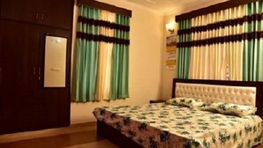 A bedroom with a bed, curtains, and a wardrobe. - Hill View Homes (Nainital)