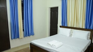A neatly made bed with white linens and two rolled towels, a wooden headboard, and a dark door in the background. - Hill View Homes (Nainital)