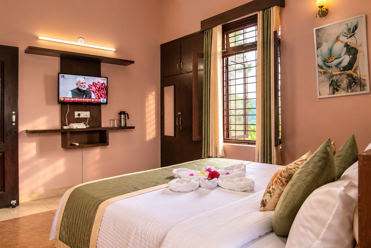 A hotel room with a bed, a TV mounted on the wall, a window with curtains, and a painting on the wall.